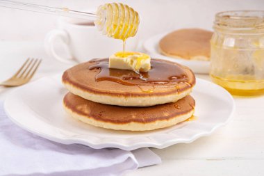 Stack of fresh baked homemade breakfast pancakes with butter and honey or maple syrup drizzles on white wooden table clipart