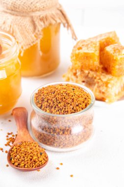 Bee pollen jar and spoon with honey and honeycomb. Trendy superfood, antioxidant organic powder, on white table background copy space clipart