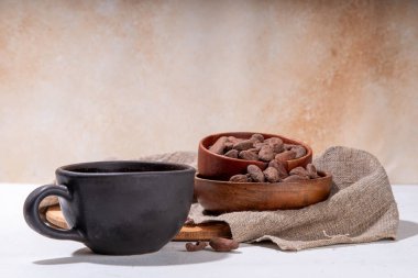 Törensel kakao içeceği. Siyah bardakta sıcak çikolata ve kakao çekirdeği. Kadın elleri kakao bardağı tutuyor. Fasulye, krema, şeker ya da malzemesiz organik çikolata içeceği.