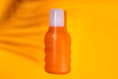 Güneş kremi maketi, plaj çantası, bayan şapkası, parmak arası terlikler ve renkli parlak arka planda tropik yapraklar. Güneş koruması, güneş kremi şişesi, yaz tatili konsepti. 