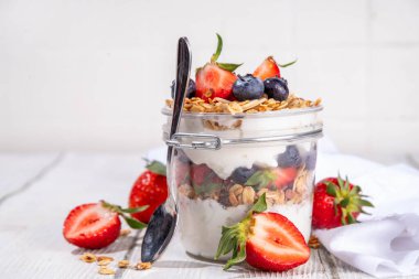 Yaz meyveleri kahvaltılık gevrek yoğurt katmanlı tatlı, yulaf taneli granola, çilek, ahşap masa arkasındaki yabanmersini fotokopi alanı.