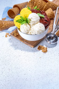 Lemon, chocolate and vanilla ice cream balls. Big bowl with ice cream scoops, on white kitchen table background with waffle cones, copy space