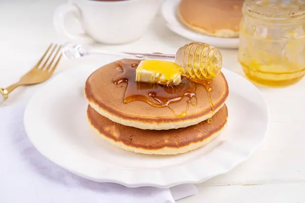stock image Stack of fresh baked homemade breakfast pancakes with butter and honey or maple syrup drizzles on white wooden table