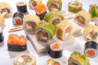 Yaratıcı Japon deniz ürünleri suşisi, suşi ruloları, maki, yemek çubuğu ve beyaz masa üzerinde silah içeren arka plan.