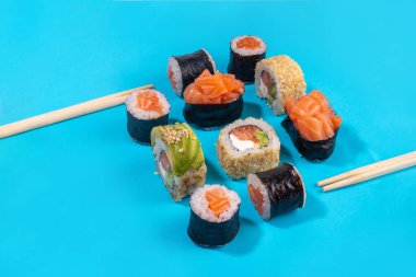 Yaratıcı Japon deniz ürünleri suşisi arka planında suşi ruloları, maki, çubuklu Gunkanlar ve parlak mavi bir arka plan var.