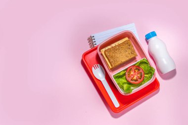 Healthy school meal, back to school concept. Children packed lunch box with balanced diet snack food - yogurt, cereal toast sandwich, apple, fresh vegetable salad, high-colored bright background