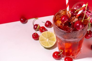 Buzlu vişneli kola, soğuk yaz meyveli alkolsüz kokteyl taze kirazlar, meyve suyu, kola ve buz, renkli arka plan fotokopi alanı.