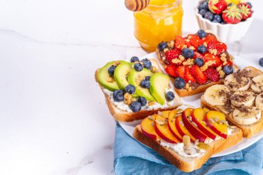 Meyveli sandviç. Fıstık ezmeli, krem peynirli çeşitli tostlar, yaz meyveleri ve meyveli çikolata - çilek, muz, şeftali, elma, yabanmersini, lezzetli öğle yemeği