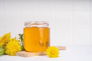 Karahindiba reçeli, kavanozda reçel ve beyaz bir masa arkasında taze karahindiba çiçekleri.