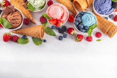 Beyaz arka planda waffle külahları ve böğürtlenlerle dolu renkli dondurmalar. Taze böğürtlenli farklı aromalı dondurma porsiyonları üst görünüm kopya alanı arka planı