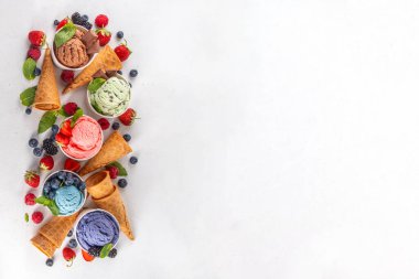 Beyaz arka planda waffle külahları ve böğürtlenlerle dolu renkli dondurmalar. Taze böğürtlenli farklı aromalı dondurma porsiyonları üst görünüm kopya alanı arka planı
