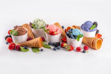 Beyaz arka planda waffle külahları ve böğürtlenlerle dolu renkli dondurmalar. Taze böğürtlenli farklı aromalı dondurma porsiyonları üst görünüm kopya alanı arka planı