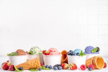 Beyaz arka planda waffle külahları ve böğürtlenlerle dolu renkli dondurmalar. Taze böğürtlenli farklı aromalı dondurma porsiyonları üst görünüm kopya alanı arka planı