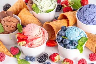 Beyaz arka planda waffle külahları ve böğürtlenlerle dolu renkli dondurmalar. Taze böğürtlenli farklı aromalı dondurma porsiyonları üst görünüm kopya alanı arka planı
