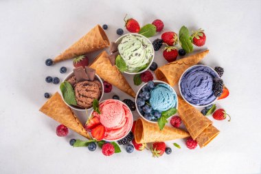 Beyaz arka planda waffle külahları ve böğürtlenlerle dolu renkli dondurmalar. Taze böğürtlenli farklı aromalı dondurma porsiyonları üst görünüm kopya alanı arka planı