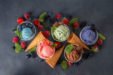Siyah arka planda waffle külahları ve böğürtlenlerle dolu renkli dondurmalar. Taze böğürtlenli farklı aromalı dondurma porsiyonları üst görünüm kopya alanı arka planı