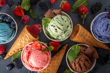 Siyah arka planda waffle külahları ve böğürtlenlerle dolu renkli dondurmalar. Taze böğürtlenli farklı aromalı dondurma porsiyonları üst görünüm kopya alanı arka planı