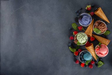 Siyah arka planda waffle külahları ve böğürtlenlerle dolu renkli dondurmalar. Taze böğürtlenli farklı aromalı dondurma porsiyonları üst görünüm kopya alanı arka planı