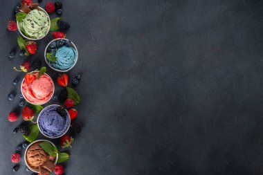 Siyah arka planda waffle külahları ve böğürtlenlerle dolu renkli dondurmalar. Taze böğürtlenli farklı aromalı dondurma porsiyonları üst görünüm kopya alanı arka planı