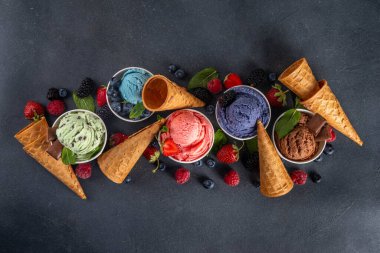 Siyah arka planda waffle külahları ve böğürtlenlerle dolu renkli dondurmalar. Taze böğürtlenli farklı aromalı dondurma porsiyonları üst görünüm kopya alanı arka planı