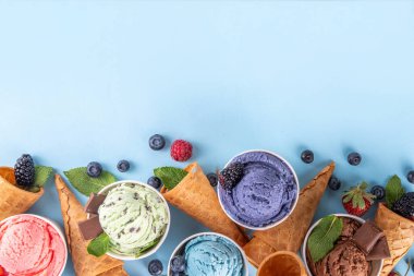 Renkli arka planda waffle konileri ve böğürtlenlerle dolu renkli, parlak dondurmalar. Taze böğürtlenli farklı aromalı dondurma porsiyonları üst görünüm kopya alanı arka planı
