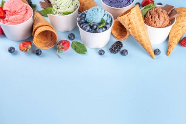 Renkli arka planda waffle konileri ve böğürtlenlerle dolu renkli, parlak dondurmalar. Taze böğürtlenli farklı aromalı dondurma porsiyonları üst görünüm kopya alanı arka planı