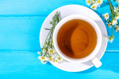 Bitkisel organik papatya çayı ve taze vahşi yaz papatya çiçekleri, beyaz fincanda, çaydanlık kopyasıyla birlikte.