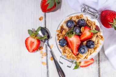 Yaz meyveleri kahvaltılık gevrek yoğurt katmanlı tatlı, yulaf taneli granola, çilek, ahşap masa arkasındaki yabanmersini fotokopi alanı.