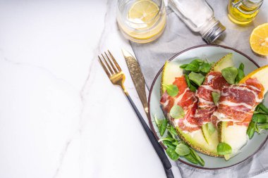 Prosciutto hamon ve yeşil yapraklı taze kavun salatası karışımı, sonbahar meyve sebze salatası, tabakta porsiyon, beyaz mermer arka plan fotokopi alanı.