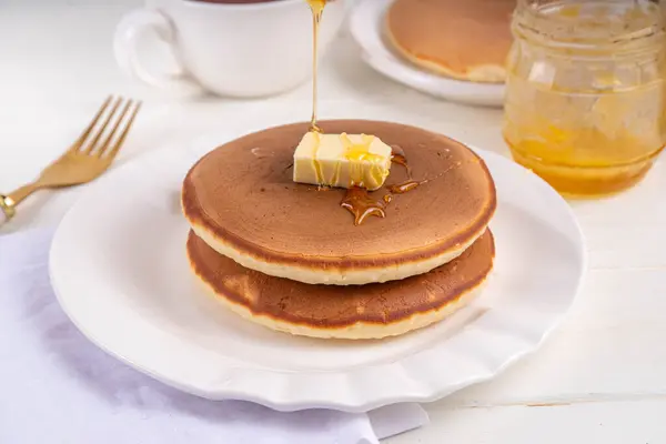 stock image Stack of fresh baked homemade breakfast pancakes with butter and honey or maple syrup drizzles on white wooden table