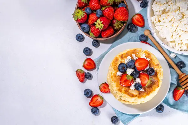 stock image Sweet homemade cottage cheese pancakes, american version of syrniki or cottage cheese fritters, big pan fried cheesy pancakes with fresh summer blueberry and strawberry, healthy high-protein breakfast