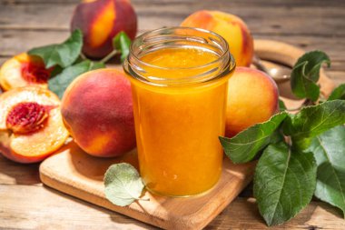 Red peach jam in small jar. Homemade autumn peach jam with fresh fruits. Fall preparations and canning on wooden table background copy space