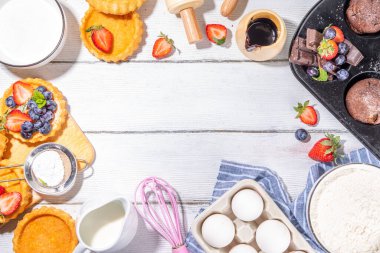 Fırında hamur işi ile yaz pişirme arka planı - çilekli kekler, mini turtalar, pişirme malzemeleri, un, yumurta, merdane, krema sütü, şeker, çilek, beyaz ahşap zemin