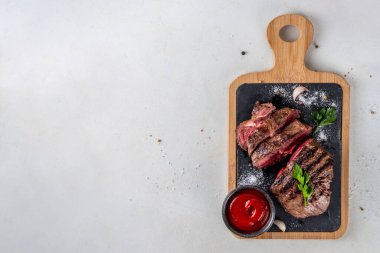 Ahşap kesme tahtasında ızgara biftek, ketçap sosu ve baharat, üst görünüm kopya alanı.