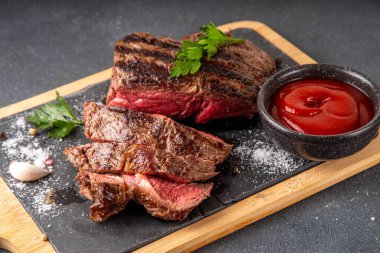 Ahşap kesme tahtasında ızgara biftek, ketçap sosu ve baharat, üst görünüm kopya alanı.