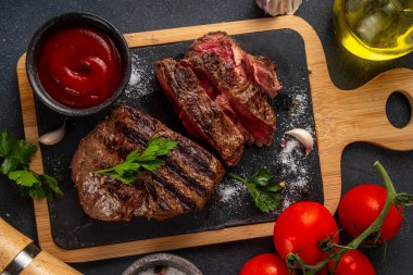 Ahşap kesme tahtasında ızgara biftek, ketçap sosu ve baharat, üst görünüm kopya alanı.