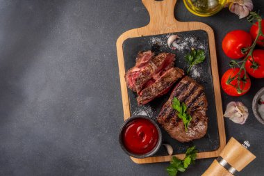 Ahşap kesme tahtasında ızgara biftek, ketçap sosu ve baharat, üst görünüm kopya alanı.