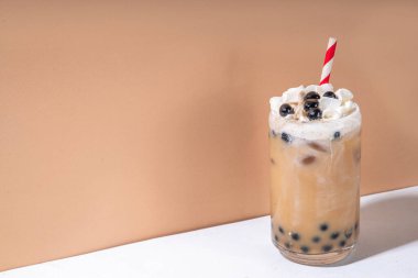 Klasik boba köpüklü çay tapyoka incileri ve sütsüz krema bardağın üstünde, yaz soğuk tatlı içeceği beyaz masa arkasında fotokopi alanı