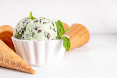 Naneli çikolatalı dondurma. Küçük porsiyonlu kase, geleneksel naneli ve çikolatalı dondurulmuş dondurma ve beyaz masada waffle konileri. 