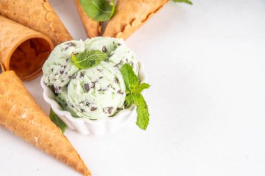 Naneli çikolatalı dondurma. Küçük porsiyonlu kase, geleneksel naneli ve çikolatalı dondurulmuş dondurma ve beyaz masada waffle konileri. 