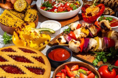 Çeşitli piknik barbekü yemekleri ve flatlay içiyorlar. Yaz bbq piknik yemekleri, ızgara etler, kebaplar, sebzeler, meyve salatası, geleneksel piknik pastası, sandviçler, üst görünüm fotokopi alanı.