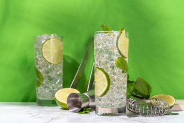 Klasik yaz soğuk mojito kokteyli, limonlu limonata, nane, ezilmiş buz ve beyaz arka planda bar aletleri.