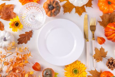 Sonbahar tatili sofrası. Şükran Günü menüsü, tebrik kartı. Tabak ve çatal bıçak takımlı beyaz mutfak masası, sonbahar yaprakları, çiçekler ve dekor düz görünüm kopya alanı