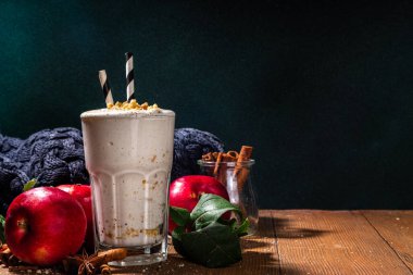 Ev yapımı elmalı turta milkshake, tart parçacıkları ve baharatlı kırmızı sonbahar elma proteini smoothie, sıcacık ahşap arka planda mevsimlik sağlıklı bir kahvaltı içeceği.