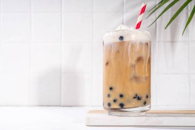 Klasik boba köpüklü çay tapyoka incileri ve sütsüz krema bardağın üstünde, yaz soğuk tatlı içeceği beyaz masa arkasında fotokopi alanı