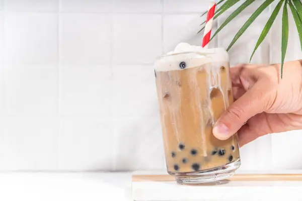 stock image Classic boba bubble tea with tapioca pearls and whipped non-dairy creamer on top of glass, summer cold sweet dessert drink on white table background copy space