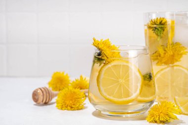 Karahindibalar soğuk buzlu çay ya da limonata. Çiçekli, karahindiba çiçeği içeceği. Çiçekler ve kökler, limon ve şurup. Arka planda beyaz masa fotokopi alanı.