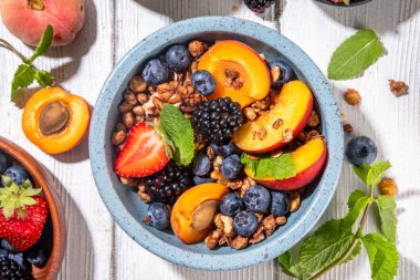 Meyve ve böğürtlenli granola kahvaltısı, yaz tatili lezzetli kahvaltı kasesi bol meyve ve böğürtlenli, süt testisi beyaz ahşap masada.