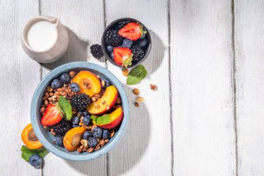 Meyve ve böğürtlenli granola kahvaltısı, yaz tatili lezzetli kahvaltı kasesi bol meyve ve böğürtlenli, süt testisi beyaz ahşap masada.