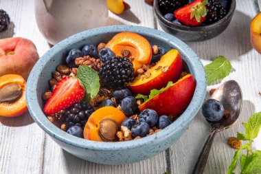 Meyve ve böğürtlenli granola kahvaltısı, yaz tatili lezzetli kahvaltı kasesi bol meyve ve böğürtlenli, süt testisi beyaz ahşap masada.